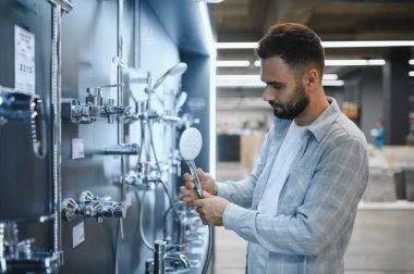Adam ev tadilatı için alışveriş yapıyor, bir nalbur reyonunda duş başlığı tutuyor.