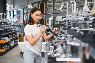 Hırdavatçıda çalışan bir kadın farklı duş başlıklarını ve banyo dekorasyonlarını inceliyor.