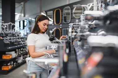 Kadın, nalbur galerisindeki modern musluğu seçiyor, banyo veya mutfak yenileme stillerini odaklanmış konsantrasyonla karşılaştırıyor