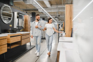 Genç bir çift, banyo için yeni mobilya ve eşyalar seçerek ev dekorasyonu mağazasında kol kola yürüyorlar.