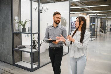 Kadın ve erkek bir hırdavatçıda ev geliştirme hakkında konuşuyor, banyo yenileme için malzeme seçiyor.