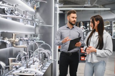 Modern bir hırdavatçıda tadilat veya tasarım sırasında müşteriye tesisat donanımı konusunda danışmanlık yapıyor.