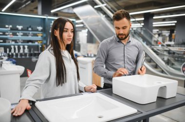 Kadın ve satıcı, yenileme seçeneklerini göz önünde bulundurarak modern bir perakende mağazasında yeni seramik lavabo seçiyorlar.