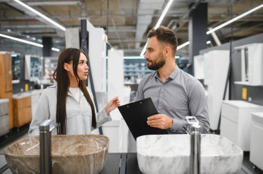 Kadın müşteri ve erkek satış asistanı modern bir hırdavatçı dükkanında yenileme için mermer lavaboları tartışıyorlar.