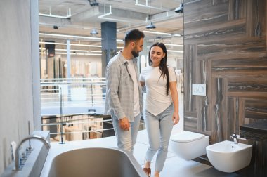 Genç bir çift banyo galerisini keşfediyor, yeni banyo küvetleri, tuvaletler ve ev geliştirme projeleri için bidet seçiyorlar.
