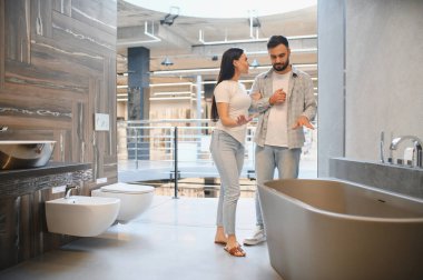 Genç çift yeni bir banyo küveti seçiyor. İnsanlar tuvaletleri, taharet musluklarını, tuvaletleri ve fayansları seçiyorlar.