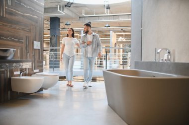 Modern bir banyo galerisini keşfeden genç bir çift, yeni küvetler, tuvaletler ve yenileme için diğer şeyleri seçiyorlar.