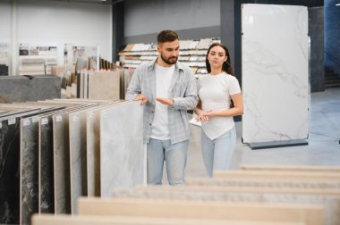 Genç çift sergi salonunda seramik seramik örnekleri karşılaştırıyor, yeni apartman tasarımı için döşeme ve ev yenileme kararları planlıyor