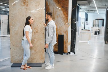 Genç çift modern bir inşaat malzemeleri mağazasında taş, granit ya da porselen seçiyor.