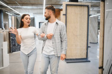 Bir sergi salonundaki döşeme ve duvar fayanslarını karşılaştıran genç bir çift, ev dekorasyonu için iç tasarım planlıyorlar.