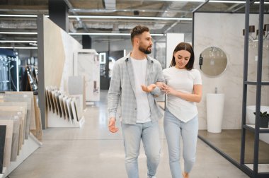 Ev dekorasyonu galerisinde yürüyen, döşeme döşemelerini ve banyo dekorasyonlarını gezen çift.