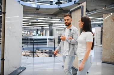 Ev geliştirme galerisinde yürüyen bir çift, yenileme projesi için geniş format fayanslarını tartışıyor.