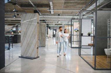 Geniş sergi salonunda yürüyen genç bir çift, tadilat için fayans seçiyorlar. Tasarım ve kaliteye odaklan