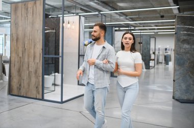 Genç bir çift, banyo tadilatı için fayans seçerek ve seçenekleri tartışarak ev geliştirme galerisinde yürüyor.