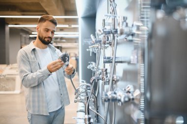 Adam duş başlığını tutuyor ve inceliyor, banyo malzemeleri ve modern bir galeride ev dekorasyonu ürünleri alıyor.