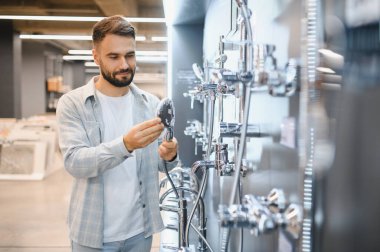 Adam duş başlığını inceliyor, bir ev geliştirme mağazasında tesisat malzemeleri alıyor, banyo yenileme planları yapıyor.