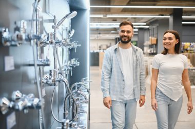 Genç bir çift modern bir hırdavatçıda yürüyor, ev yenileme için yeni hijyenik malzeme ve duş sistemleri seçiyorlar.