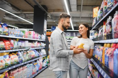 Gülümseyen genç bir çift, marketin koridorundaki raflardan daha temiz bir ürün seçiyor.