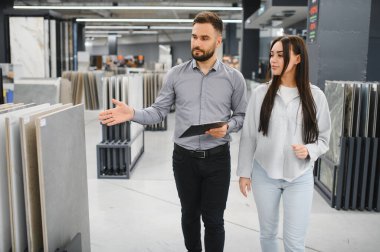 İnşaat malzemeleri dükkanında ev yenileme projesi için yeni döşeme ya da duvar döşemesi seçen kadına perakende işinde yardım edin