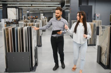 Erkek satış asistanı ve kadın müşteri seramik zemin ve duvar fayanslarına bakıyor.