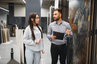 Modern bir hırdavatçıda kadın bir alıcıya fayans seçeneklerini açıklayan satıcı. Ev geliştirme malzemeleri alışverişi