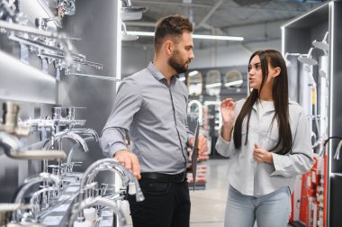 Kadın alıcı, modern bir hırdavatçıda bir erkek satıcıyla tesisat seçeneklerini tartışıyor, yeni banyo malzemeleri alıyor.