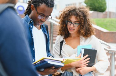 Diverse young students standing on campus, holding textbooks and notebooks, engaging in a discussion