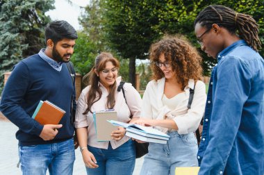 Diverse group of students standing outdoors on a university campus, smiling and discussing educational books, fostering friendship