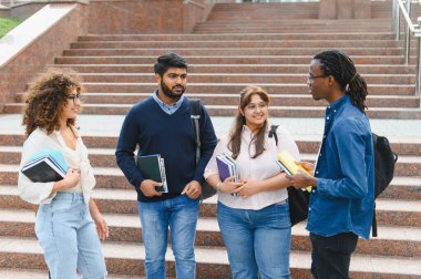 Çeşitli yetişkin öğrenciler kitap ve çanta taşıyorlar, üniversite merdivenlerinde duruyorlar ve konuşuyorlar.