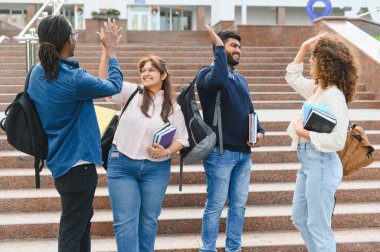 Çeşitli üniversite öğrencileri kampüste beşlik çakıyor ve gülümsüyor, başarıyı ve arkadaşlığı kutluyor.