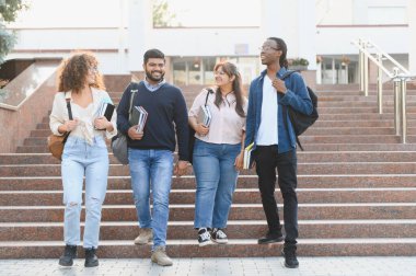 Çeşitli üniversite öğrencileri gülerek kampüs merdivenlerinde kitap ve sırt çantaları taşıyarak eğitime odaklanıyorlar.