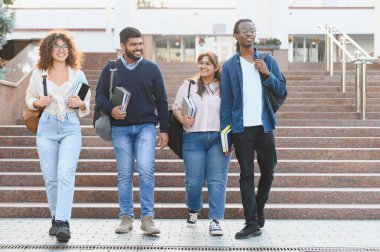 Çeşitli üniversite öğrencileri kampüs merdivenlerinden aşağı iniyor, ellerinde kitaplar ve sırt çantalarıyla, eğitim ve arkadaşlığı temsil ediyorlar.