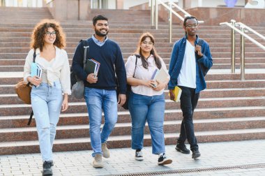 Bir grup çok ırklı üniversite öğrencisi kampüs merdivenlerinde birlikte yürüyor, ellerinde kitaplar ve sırt çantaları, eğitimi ve arkadaşlığı temsil ediyorlar.