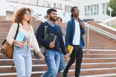 Kampüs merdivenlerinde ellerinde kitap ve sırt çantalarıyla gezen çeşitli üniversite öğrencileri eğitim ve arkadaşlığı temsil ediyor.