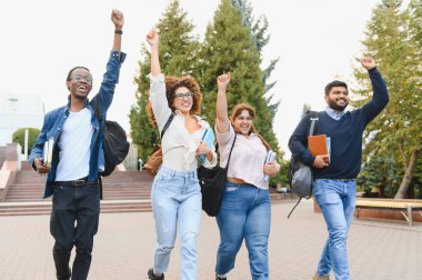 Heyecanlı üniversite öğrencilerinden oluşan bir grup kutlama için kollarını kaldırıyor, üniversite kampüsünde yürüyor, başarıyı, arkadaşlığı ve çeşitliliği somutlaştırıyorlar.