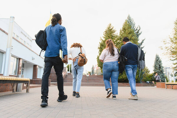 Diverse students with backpacks walking away on a university campus path, heading towards a building during daytime