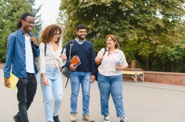 Üniversite kampüsünde birlikte yürüyen mutlu çoklu etnik öğrenciler eğitim ve arkadaşlığı temsil eden kitaplar ve sırt çantaları taşıyorlar.