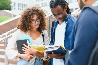 Çeşitli üniversite öğrencileri akademik materyalleri tartışıyor ve kampüs merdivenlerinde dururken çalışmalar üzerinde işbirliği yapıyorlar.