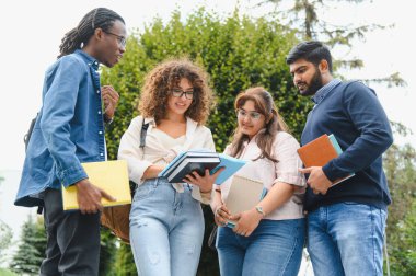 Üniversite kampüsünde açık havada duran çeşitli genç öğrenci grupları tartışmalar yapıyor ve kitap tutuyorlar.