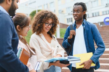 Bir üniversite kampüsünde ders kitaplarını tutan çeşitli üniversite öğrencileri bir araya gelip öğreniyorlar.