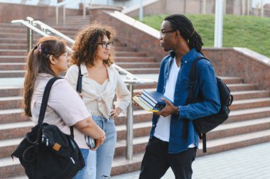 Çeşitli genç öğrenciler üniversite kampüsünün merdivenlerinde dikilip sohbet ediyorlar, gelecekteki eğitim ve çalışmalarını tartışıyorlar.