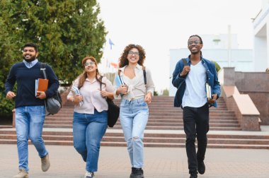 Diverse group of multiracial university students walking and smiling on campus with books and backpacks, representing education and friendship