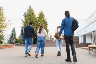 Group of multiethnic high school or college students with backpacks and books walking across campus on a sunny day