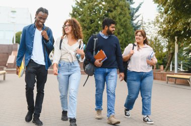 Sırt çantaları ve kitaplar taşıyan, üniversite kampüsünde gezen, üniversite hayatının tadını çıkaran çeşitli gülümseyen öğrenciler.