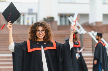 Young woman smiling, raising diploma and mortarboard, celebrating academic achievement and success after graduation
