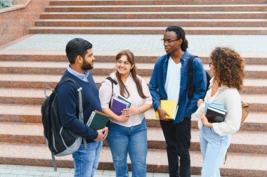 Diverse university students talking and smiling on campus stairs, carrying books and backpacks. Showing friendship, education, and learning