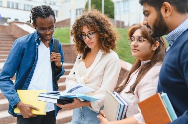 Group of diverse university students collaborating, discussing, and learning with books and notebooks on campus stairs