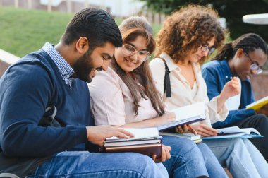 Diverse group of young students collaborating and studying books on a university campus outdoors, enjoying learning and education