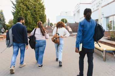 Group of diverse university students with backpacks walking on campus, heading towards a building for their classes and studies