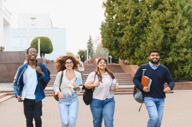 Group of multiethnic young adults walking on a university campus, carrying books and backpacks. Education and friendship concept